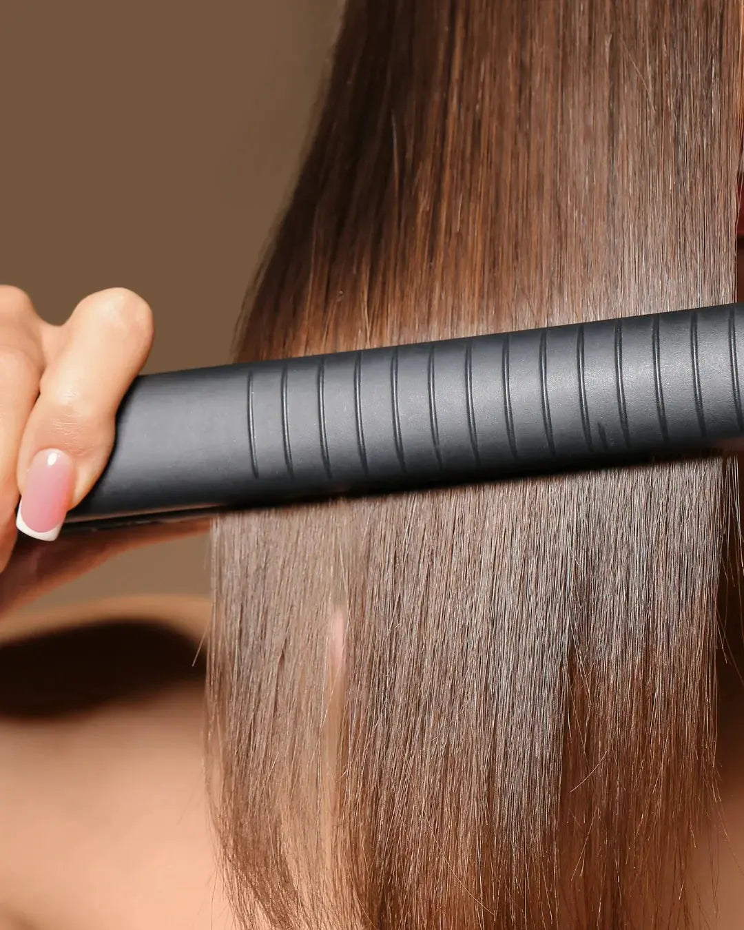 femme avec de beaux cheveux brillants qui se lisse les cheveux avec un lisseur noir